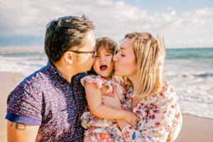 parents kiss their child on a maui beach