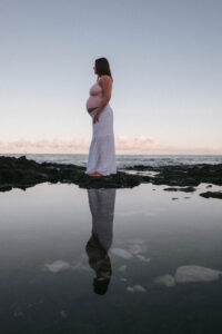 Kona Babymoon - pregnant woman standing on the rocks with her reflection in the ocean.