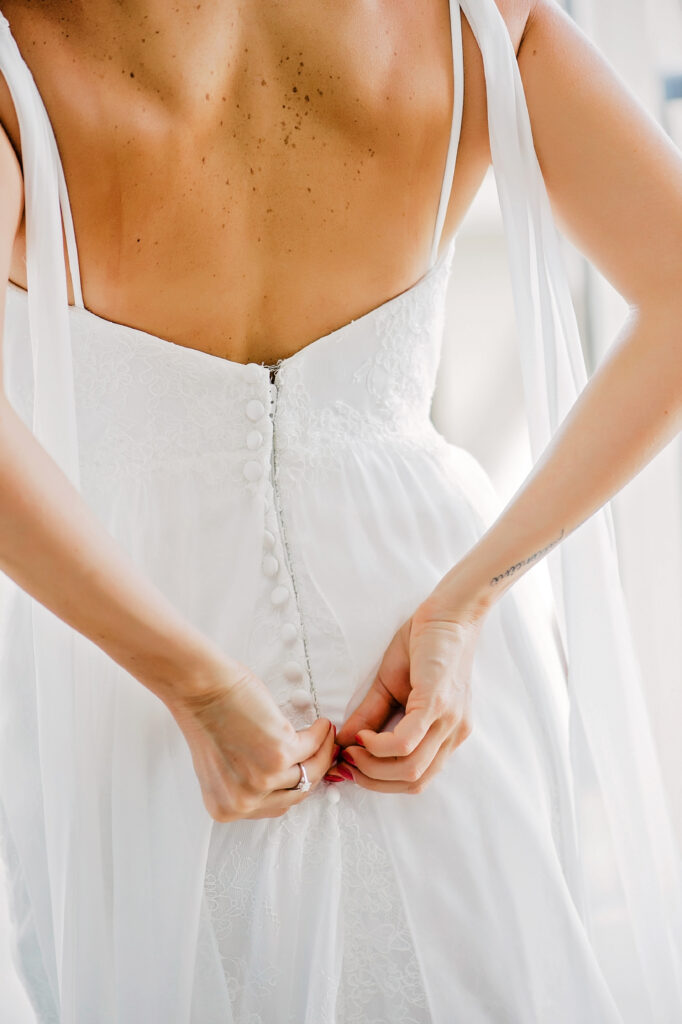 Bride delicately buttons her gown, preparing for her intimate elopement.
