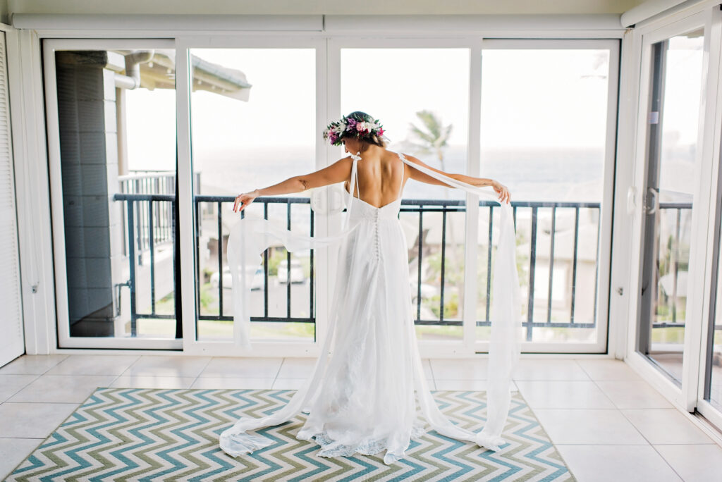 Bride stands on a balcony, holding both ends of her gown while getting ready for her elopement.