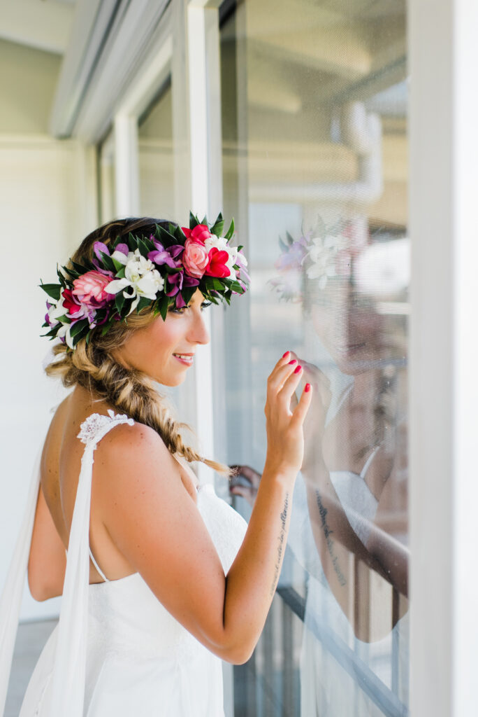 Bride stands by the window, holding the glass and smiling, glowing with joy on her special day.