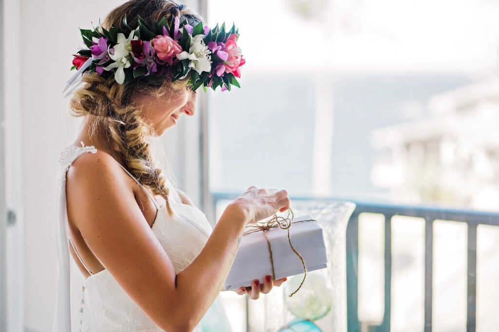 The bride stands on a balcony, holding a gift while smiling before her elopement.