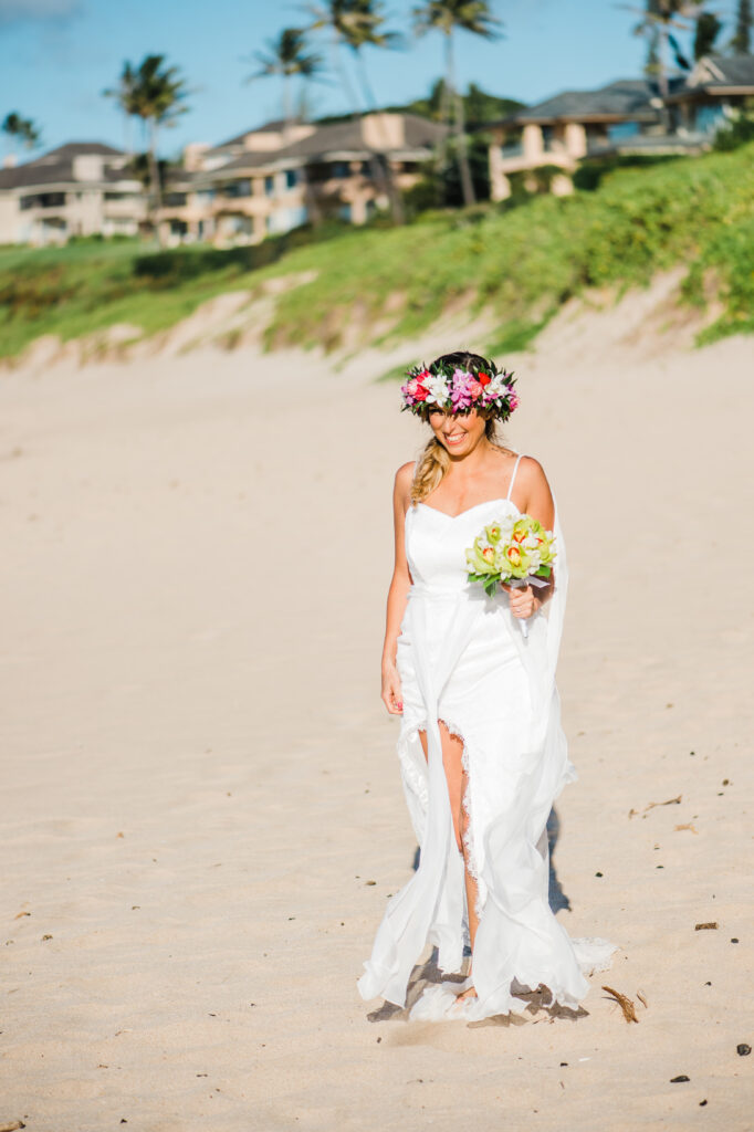 The bride walks barefoot in the sand, holding her bouquet.