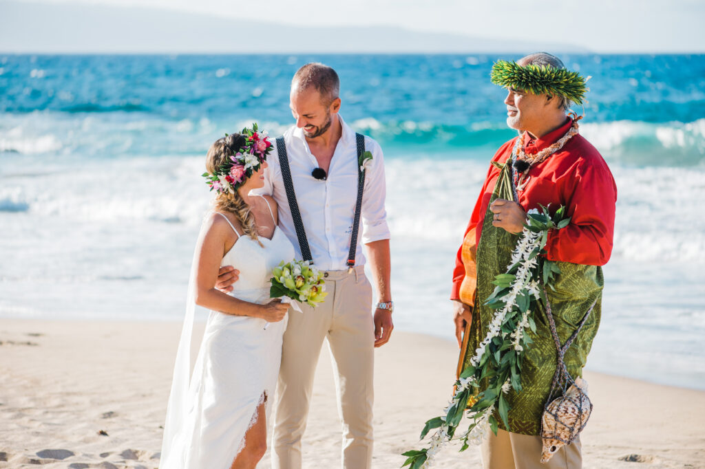 The couple exchanges heartfelt smiles during their intimate beach ceremony, with the Hawaiian officiant.