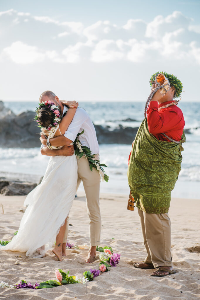 The couple leans in for a kiss while the Hawaiian officiant blesses their union.