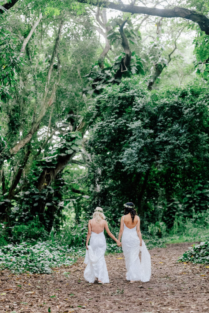 The brides walk side by side along a peaceful forest path, celebrating their Maui micro wedding.
