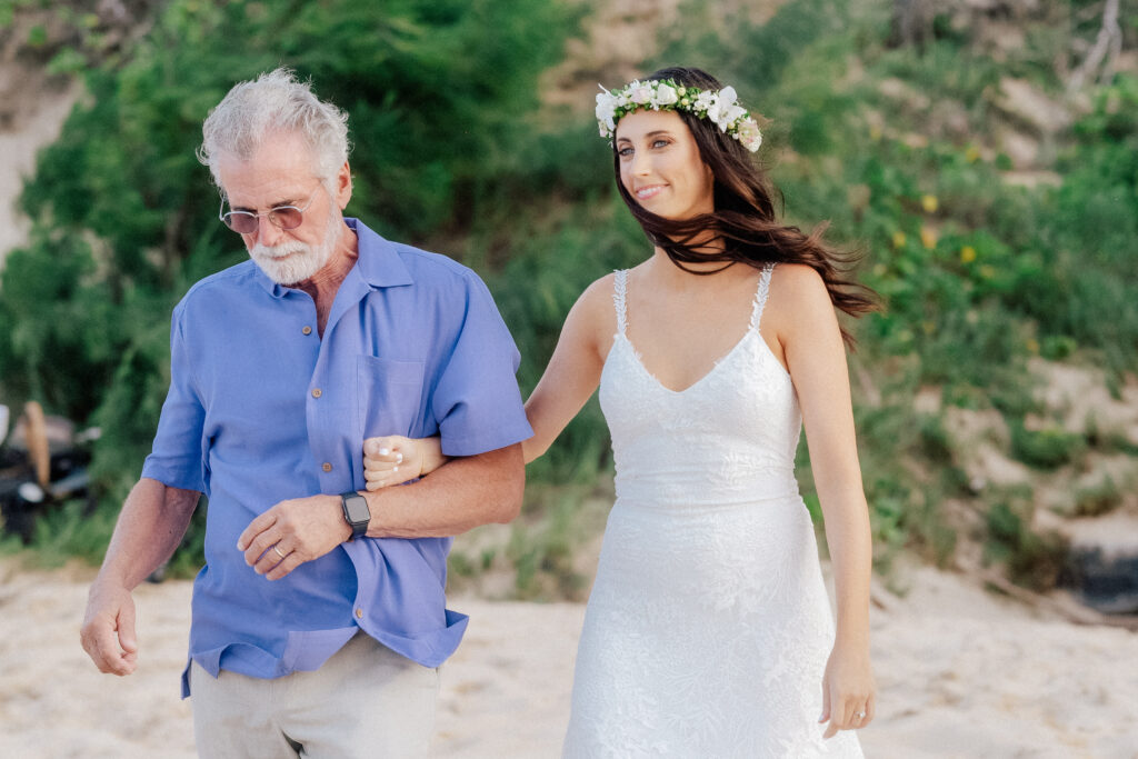 Bride escorted through the tropical scenery, a heartfelt start to the beach ceremony.