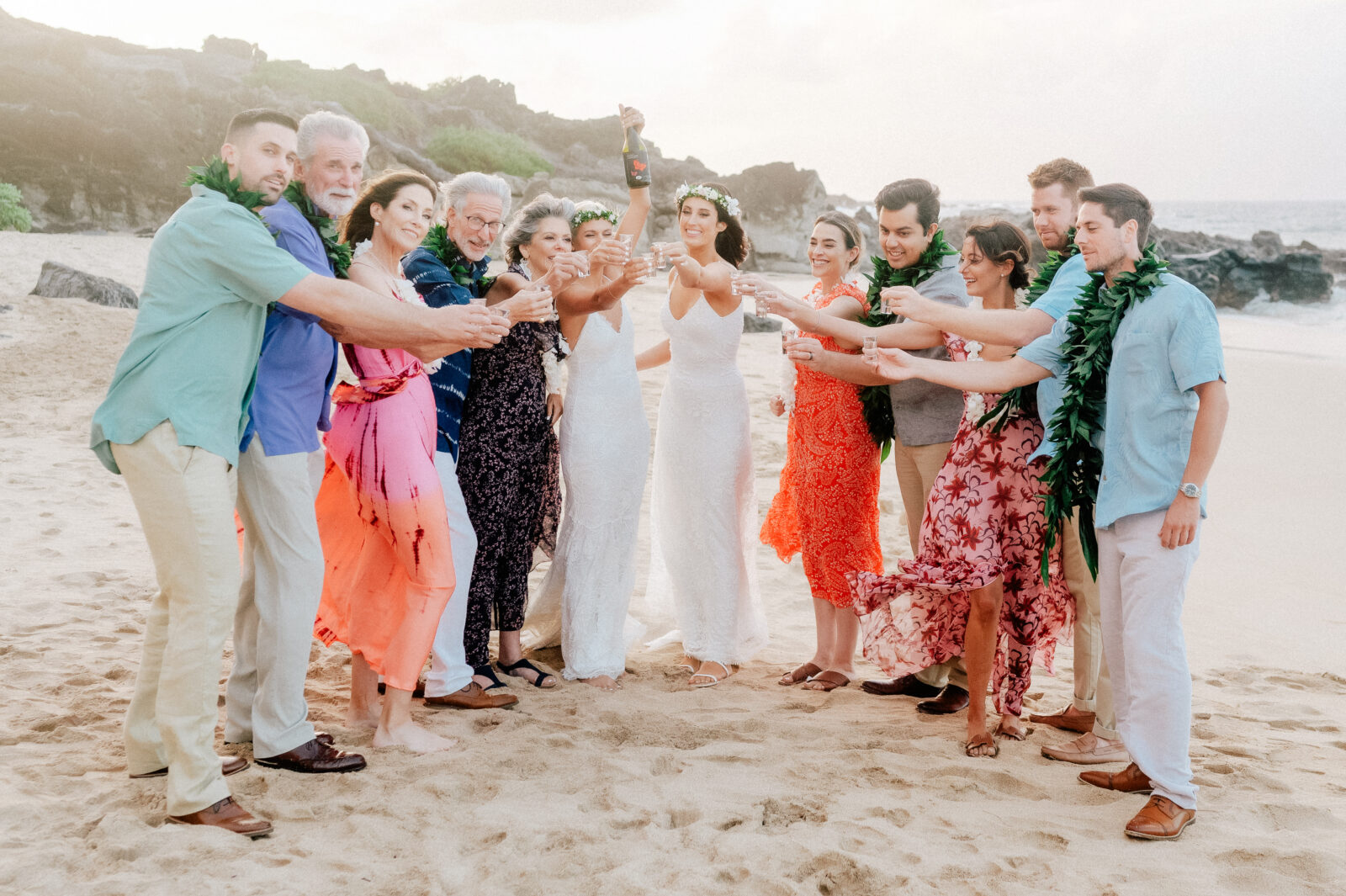 A joyful group portrait of the couple with family and friends on Ironwood Beach, Maui.
