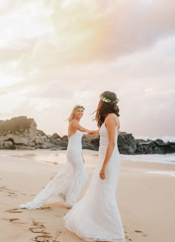 The brides walk along the shore, soaking in the golden light of their Maui elopement.