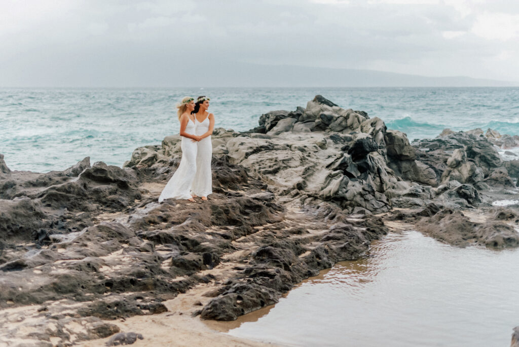 A stunning bride stands atop Maui’s rocky coastline, waves crashing below.