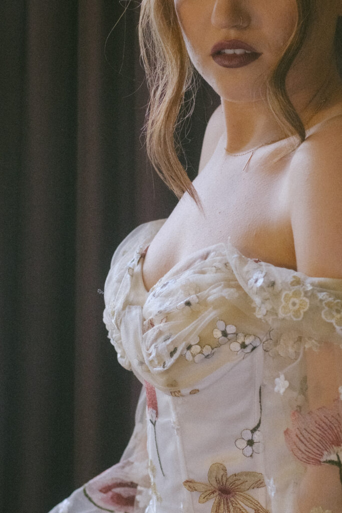 Bride’s dress close-up, revealing intricate floral beading and off-shoulder design in soft lighting.