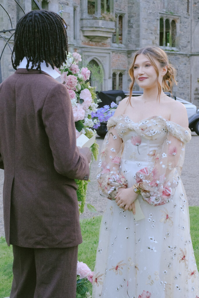 Bride and groom stand facing each other, sharing a private, heartfelt moment outdoors.