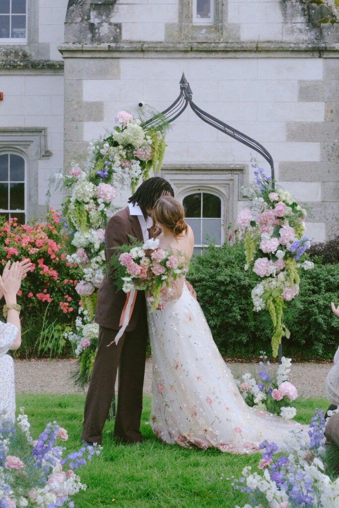 Bride and groom kissed under a floral arch with Wilton Castle in the backdrop.