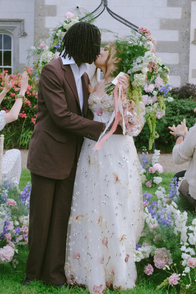 Bride and groom kisses under a floral arch with Wilton Castle in the backdrop.