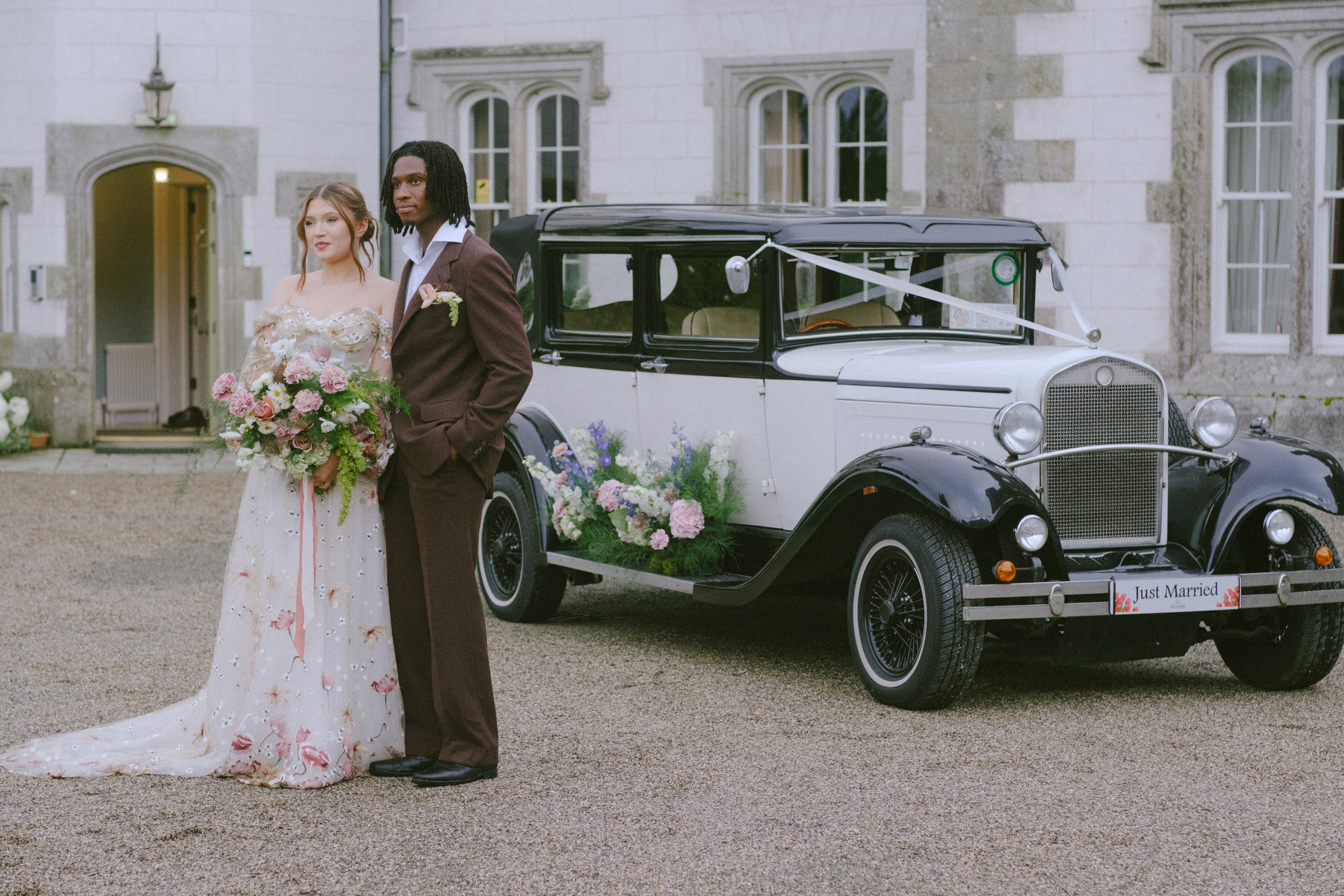 Bride and groom beside a vintage car, surrounded by romantic floral arrangements at Wilton Castle.