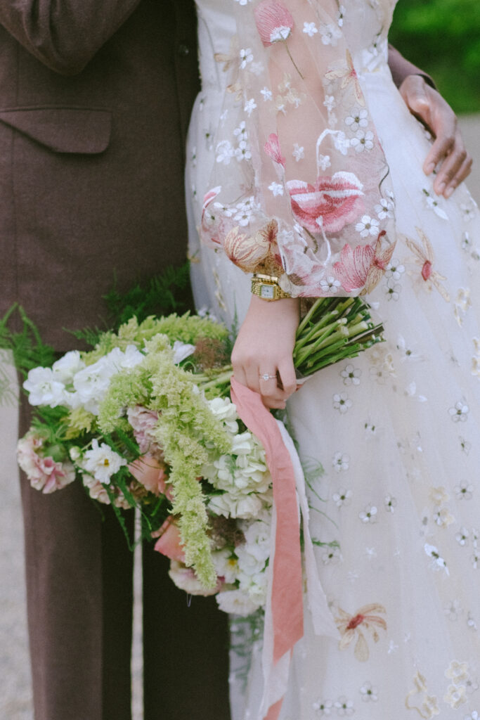 Bride holding a lush bouquet with pink and green tones, showcasing intricate dress details.