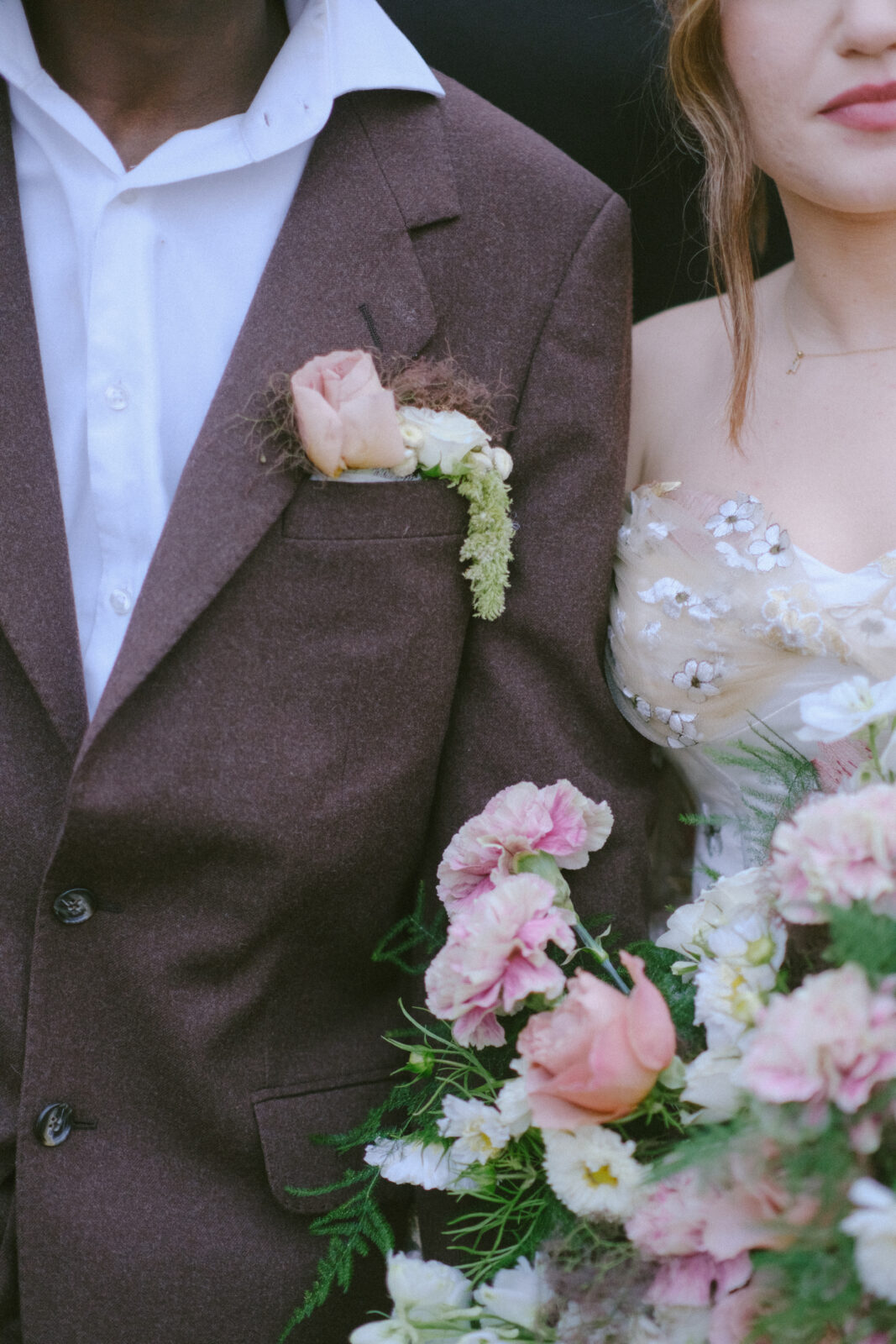 Groom’s lapel close-up with boutonniere and bride holding a pastel floral bouquet.