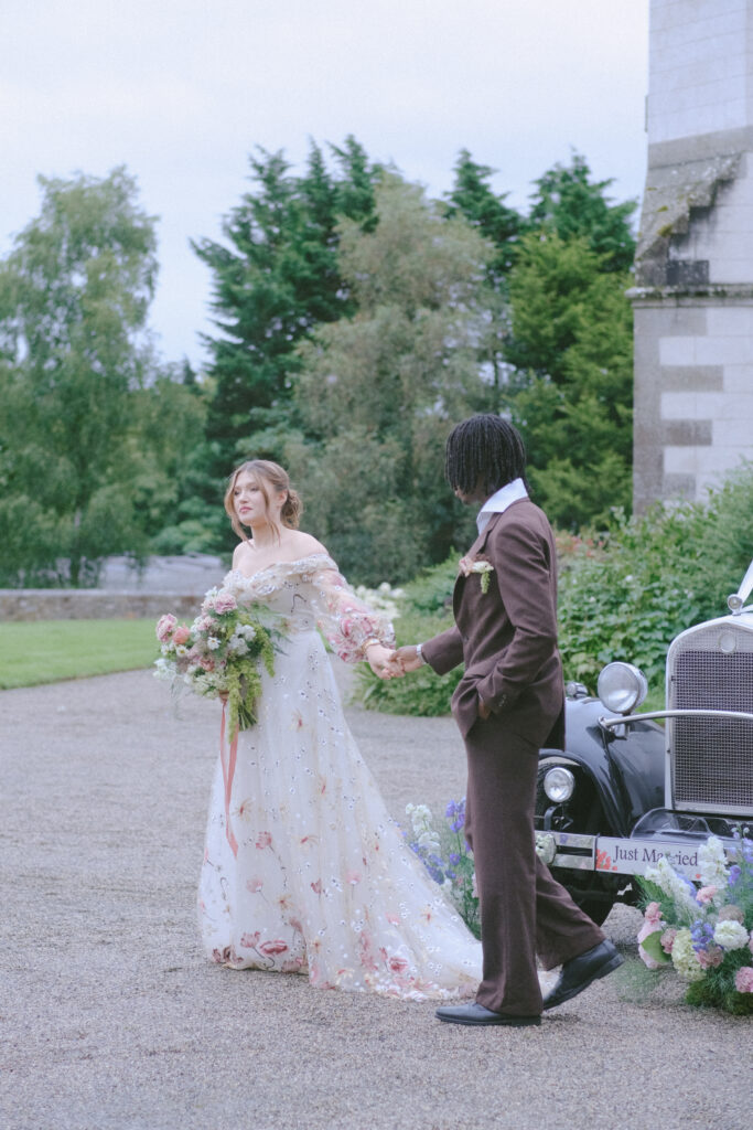 Bride walks toward the groom holding her bouquet, a cinematic scene framed by lush greenery.